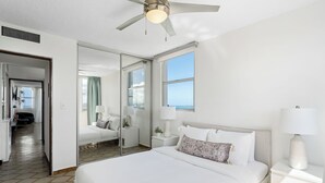 Habitació d'hotel amb un llit gran, un ventilador de sostre, una finestra amb vistes i una porta que dona a una altra habitació.
