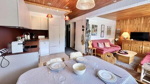 A cozy living room with a dining table set for four, a kitchen area, a red sofa, and a television. - 50m from ski slopes, 4th floor, view swimming pool/mountain, ski locker, 45m², Vars (Vars)