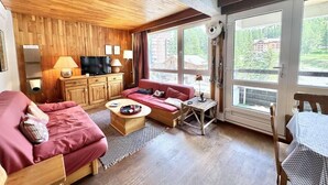 A cozy room with a wooden ceiling, a red sofa, a wooden table, and a TV on a wooden cabinet. - 50m from ski slopes, 4th floor, view swimming pool/mountain, ski locker, 45m², Vars (Vars)