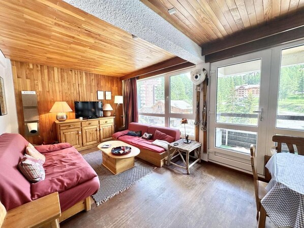 A cozy room with a wooden ceiling, a red sofa, a wooden table, and a TV on a wooden cabinet.