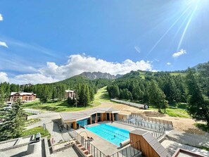 A swimming pool area with a view of mountains and a ski slope in the background.