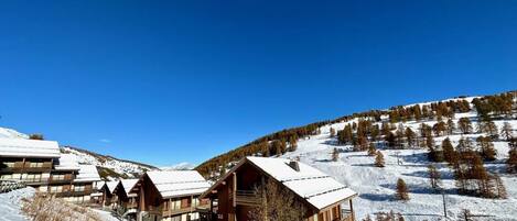 A snow-covered lodge with multiple wooden cabins, a ski lift, and a mountainous backdrop.