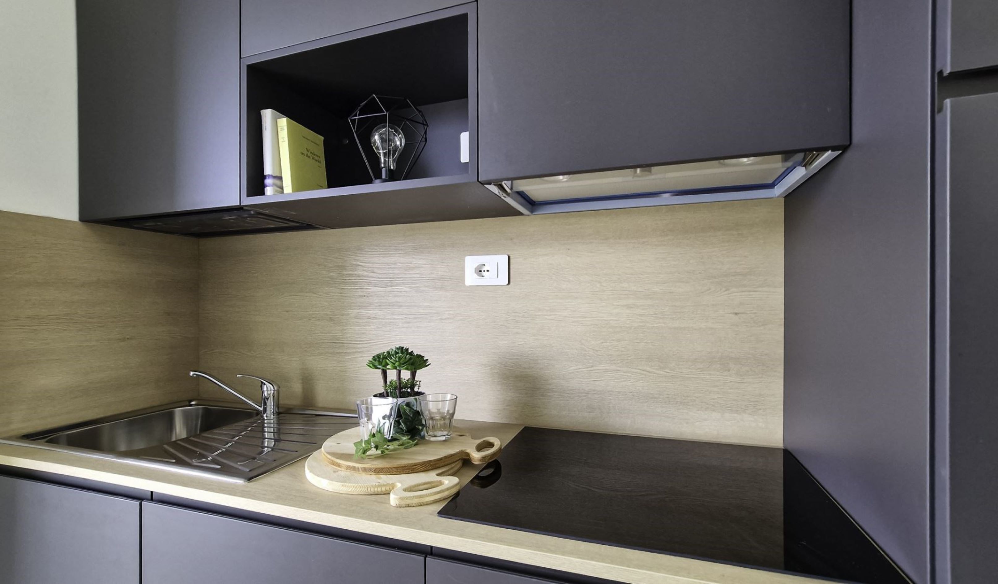 A modern kitchen with a stainless steel sink, a built-in oven, and a small shelf above the counter.