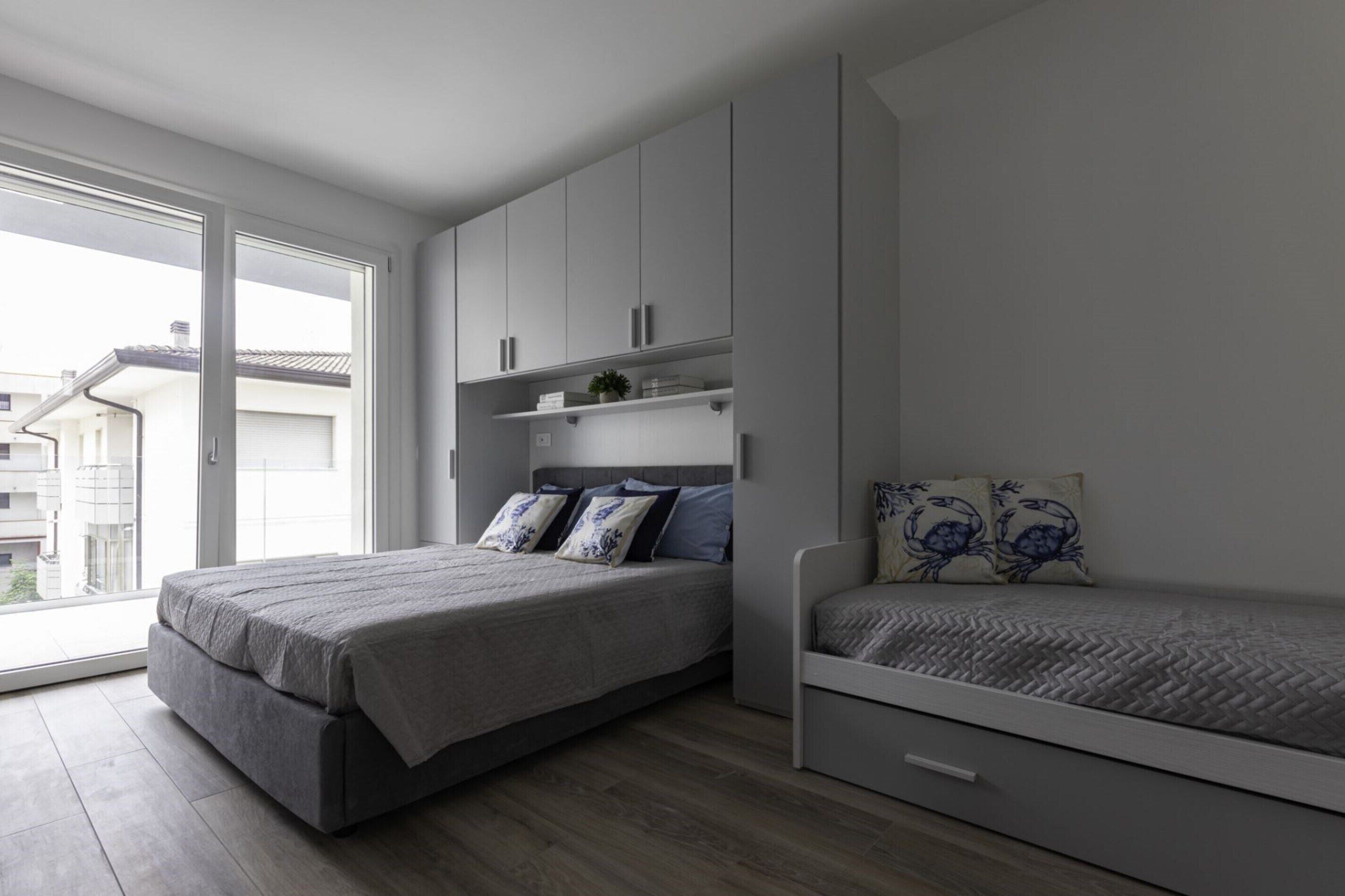 Ein modernes Schlafzimmer mit einem großen Bett, einem kleineren Bett und integrierten Stauraum.