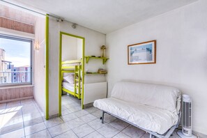 Una habitación con literas, un sofá, un radiador, un cuadro en la pared y una ventana con vistas a edificios.