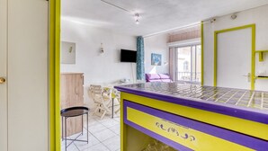 A room with a purple and yellow table, a chair, a TV, and a window. - Apartment 'Sur Le Port' with Sea View and Private Garden (Agde)