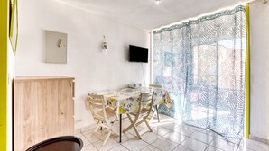A dining area with a table, chairs, a television, and a patterned curtain. - Apartment 'Sur Le Port' with Sea View and Private Garden (Agde)