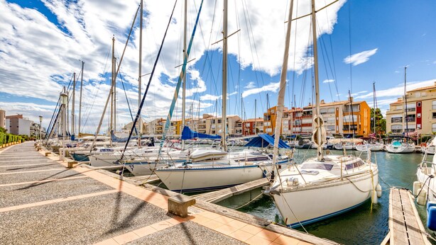 A marina with multiple boats docked, a waterfront promenade, and buildings in the background. - Apartment 'Sur Le Port' with Sea View and Private Garden (Agde)