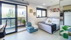 A modern hotel room with a bed, a small seating area, a balcony with a view of the city, and a refrigerator. - Vila Mariana perto do metrô AC (Sao Paulo)