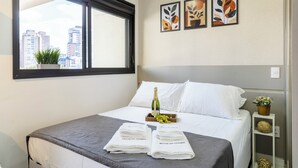 A hotel room with a bed, a window with a view of buildings, and three framed artworks on the wall. - Vila Mariana perto do metrô AC (Sao Paulo)