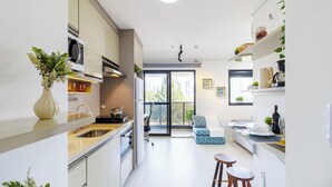 A modern kitchen with a built-in oven, a sink, and a dining area with stools. - Vila Mariana perto do metrô AC (Sao Paulo)