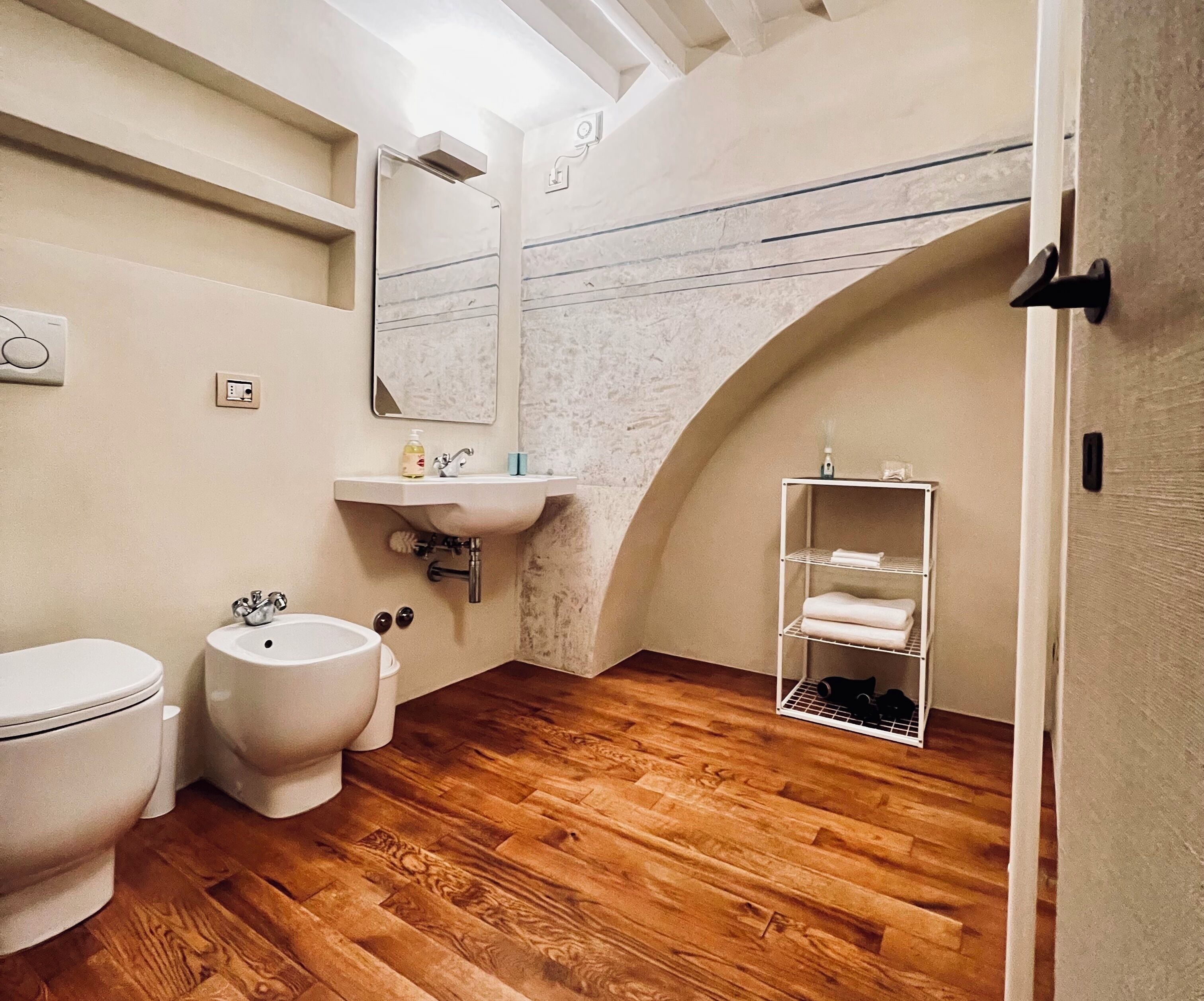 A bathroom with a wooden floor, a bidet, a sink, and a towel rack.