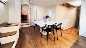 Un comedor amplio con una larga mesa y sillas negras, suelo de madera y una escalera blanca.