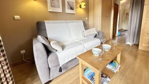 A cozy living room with a grey sofa, a wooden coffee table with magazines, and wall-mounted lamps.