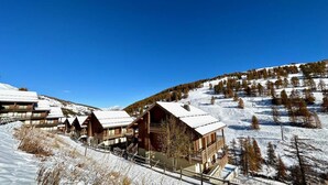A snow-covered lodge with multiple wooden cabins, a ski lift, and a mountainous backdrop.