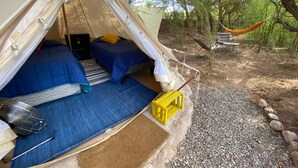 Une tente avec deux lits, une petite table et une caisse jaune.