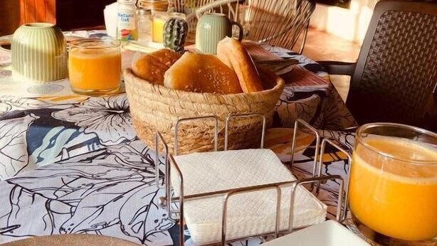 Une table mise pour le petit-déjeuner, avec du pain, du jus et un panier de viennoiseries.