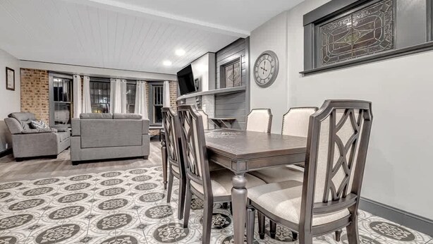 Un comedor con una mesa y sillas, un televisor sobre un mueble, un reloj en la pared y un suelo con estampado.
