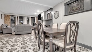 A dining area with a table and chairs, a television on a stand, a clock on the wall, and a patterned floor.