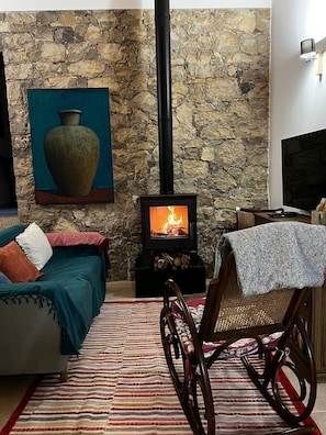 Un salon chaleureux avec un mur en pierre, une cheminée, un canapé, un fauteuil et un téléviseur.