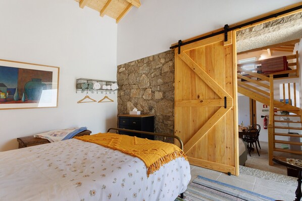 Een slaapkamer met een bed, een houten deur, een stenen muur en een trap.