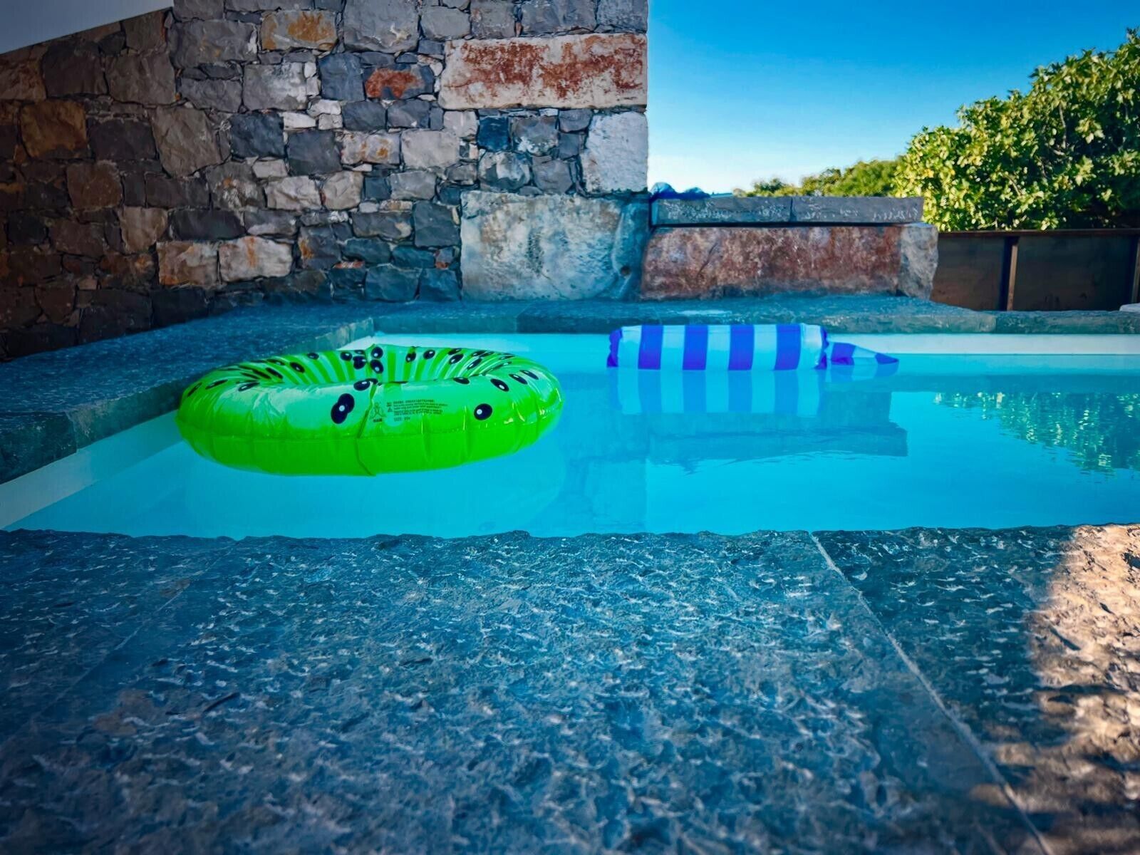 A swimming pool with a stone wall and a clear blue sky.