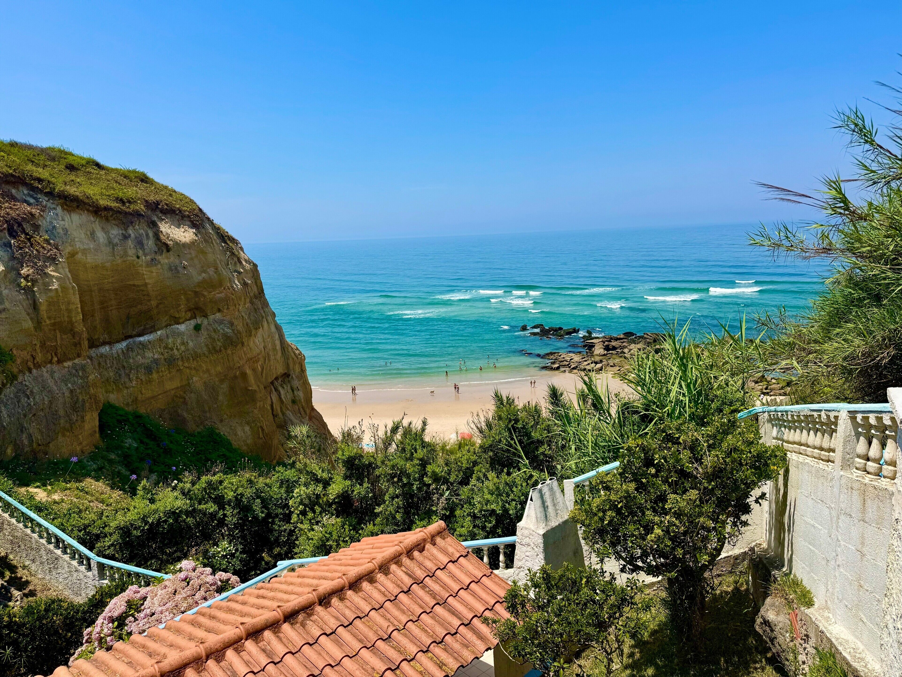 Une vue sur la côte, avec une plage, des falaises rocheuses et un bâtiment doté d’un toit en tuiles.