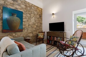 Un salon avec un mur en pierre, un téléviseur à écran plat, une bibliothèque, un canapé et un fauteuil à bascule.