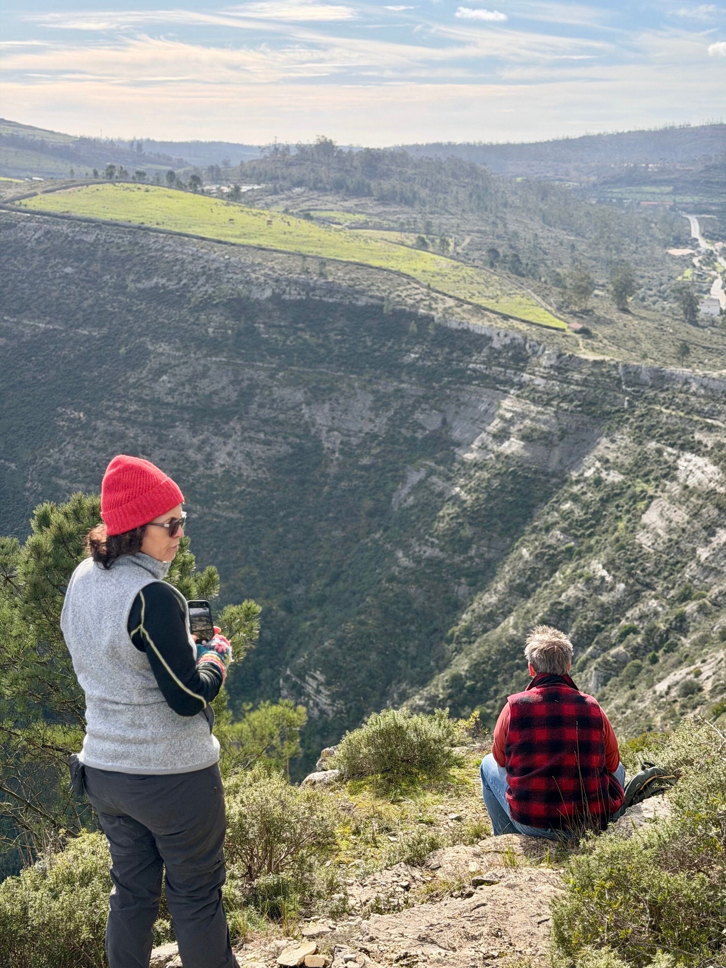 Une personne prend une photo d’une vallée, avec une route et des bâtiments visibles au loin.