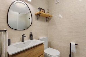 Een badkamer met een wit wastafel, een zwarte kraan, een houten wastafelmeubel, een wit toilet en een spiegel met een zwarte lijst.