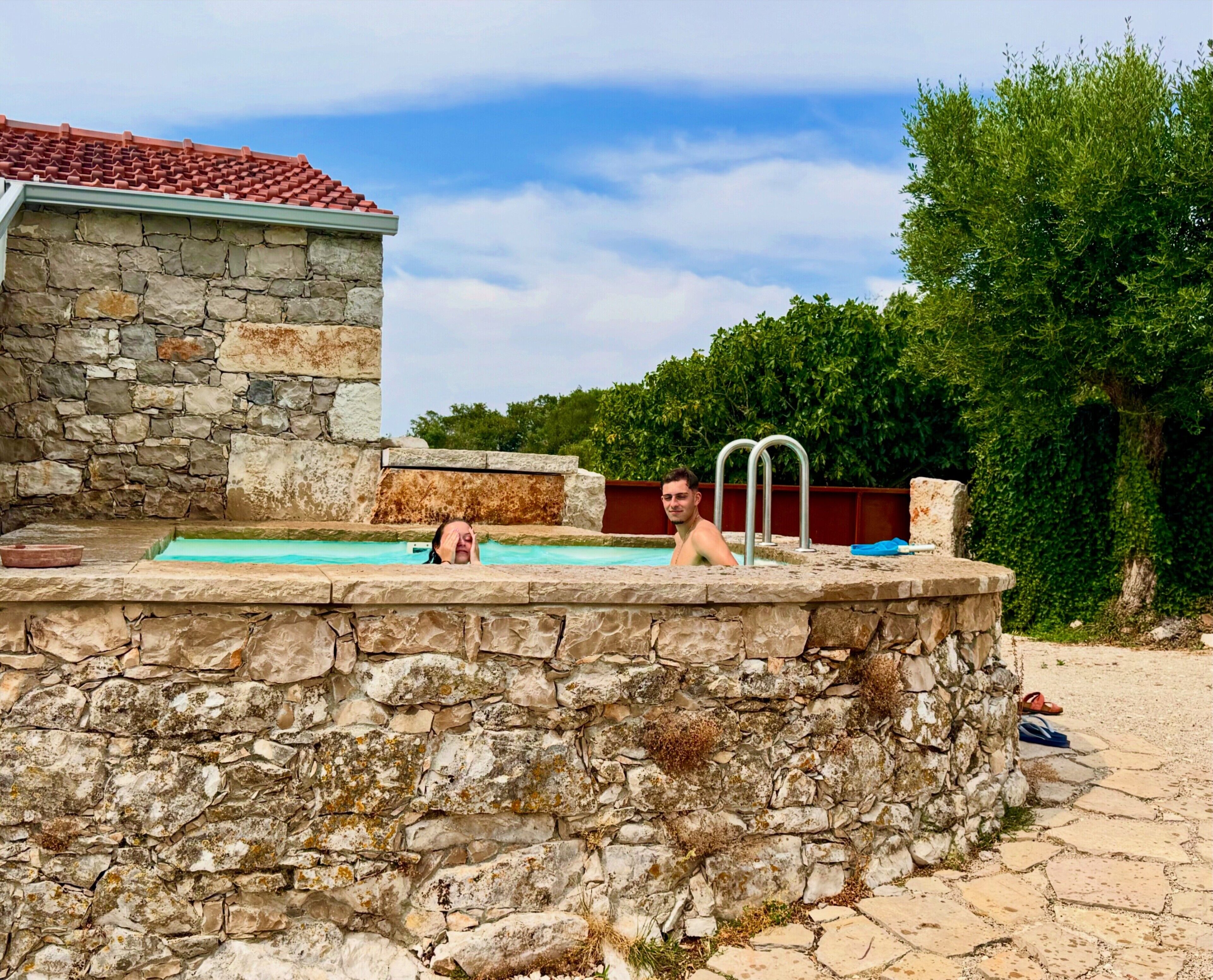 A stone pool with a stone wall, a red-tiled roof, and a metal ladder.