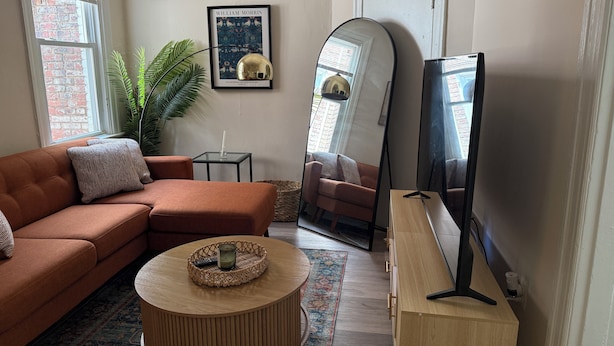 A living room with a brown sofa, a round wooden coffee table, a large mirror, and a framed picture on the wall.