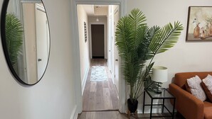 A hallway with a mirror, a potted plant, a lamp, and a sofa.