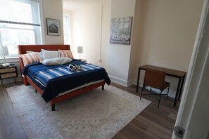 Quarto com cama, escrivaninha, cadeira, mesa de cabeceira e abajur.