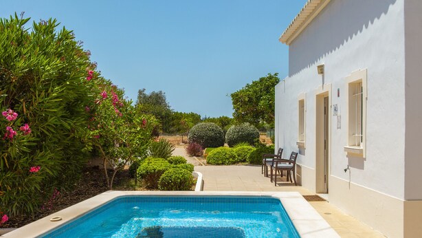 A swimming pool with a tiled edge, surrounded by greenery and a building with windows and doors. - Villa with BBQ and plunge pool in Odiáxere (Odiáxere)