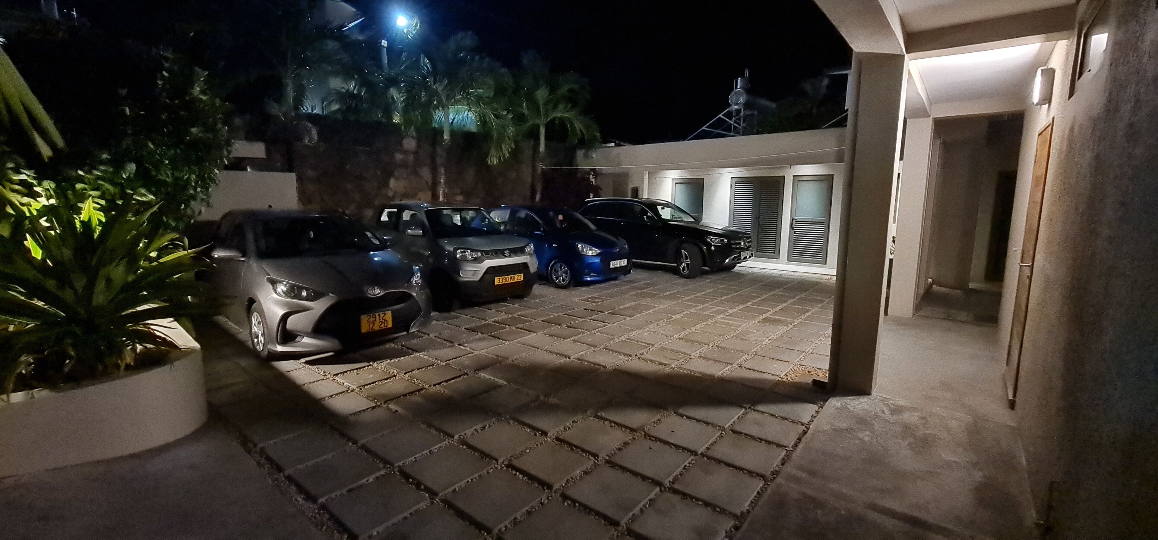 A nighttime parking area with several cars, a potted plant, and a building entrance.