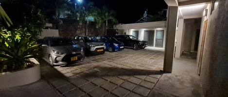 A nighttime parking area with several cars, a potted plant, and a building entrance.