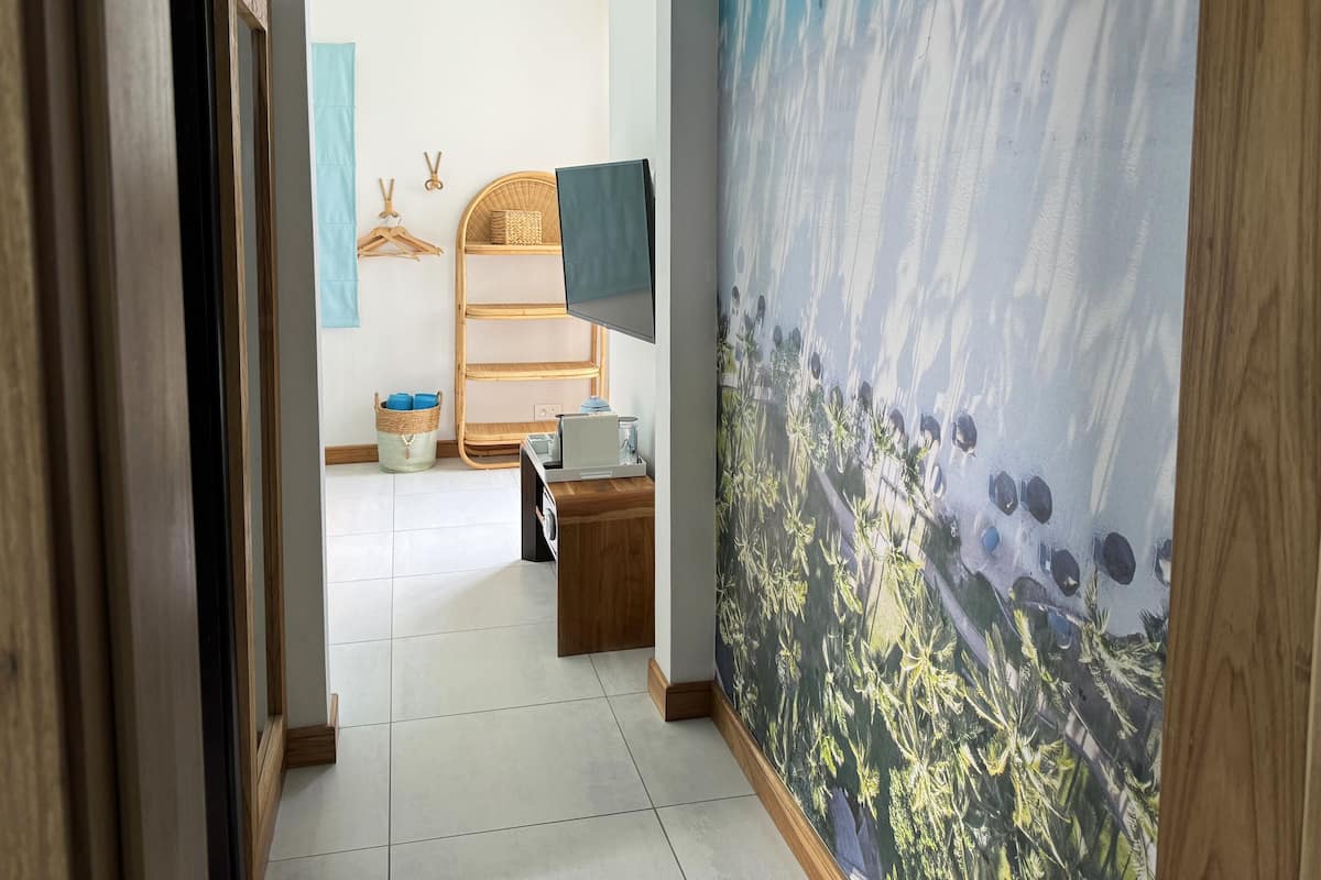 Een gang met een houten deur, een tv aan de muur, een rieten plank met manden, en een betegelde vloer.
