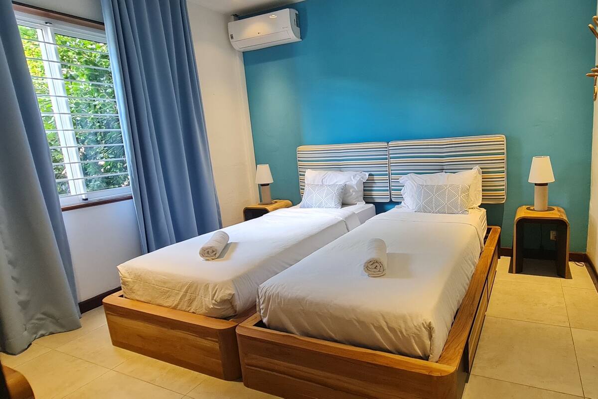 Een tweepersoonsbed met twee nachtkastjes, een raam met gordijnen en een airconditioning aan de muur.