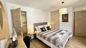 Un dormitorio moderno con una cama grande, suelo de madera, un escritorio con silla y un armario.