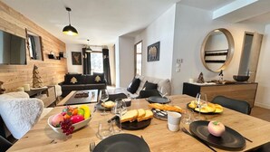 Un comedor con una mesa de madera dispuesta para una comida, un frutero y una manzana decorativa en un plato.