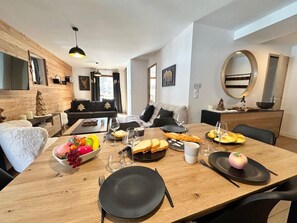 Ruokailutila, jossa on puinen ruokapöytä katettuna, hedelmäkulho ja koristeomena lautasella.