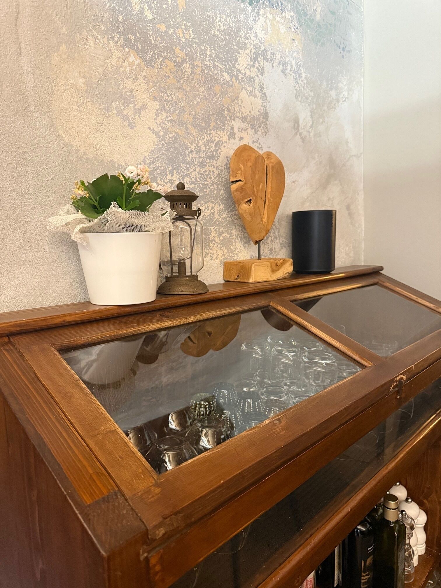 Un mueble de madera con una superficie de cristal que contiene varios vasos y una planta en maceta.