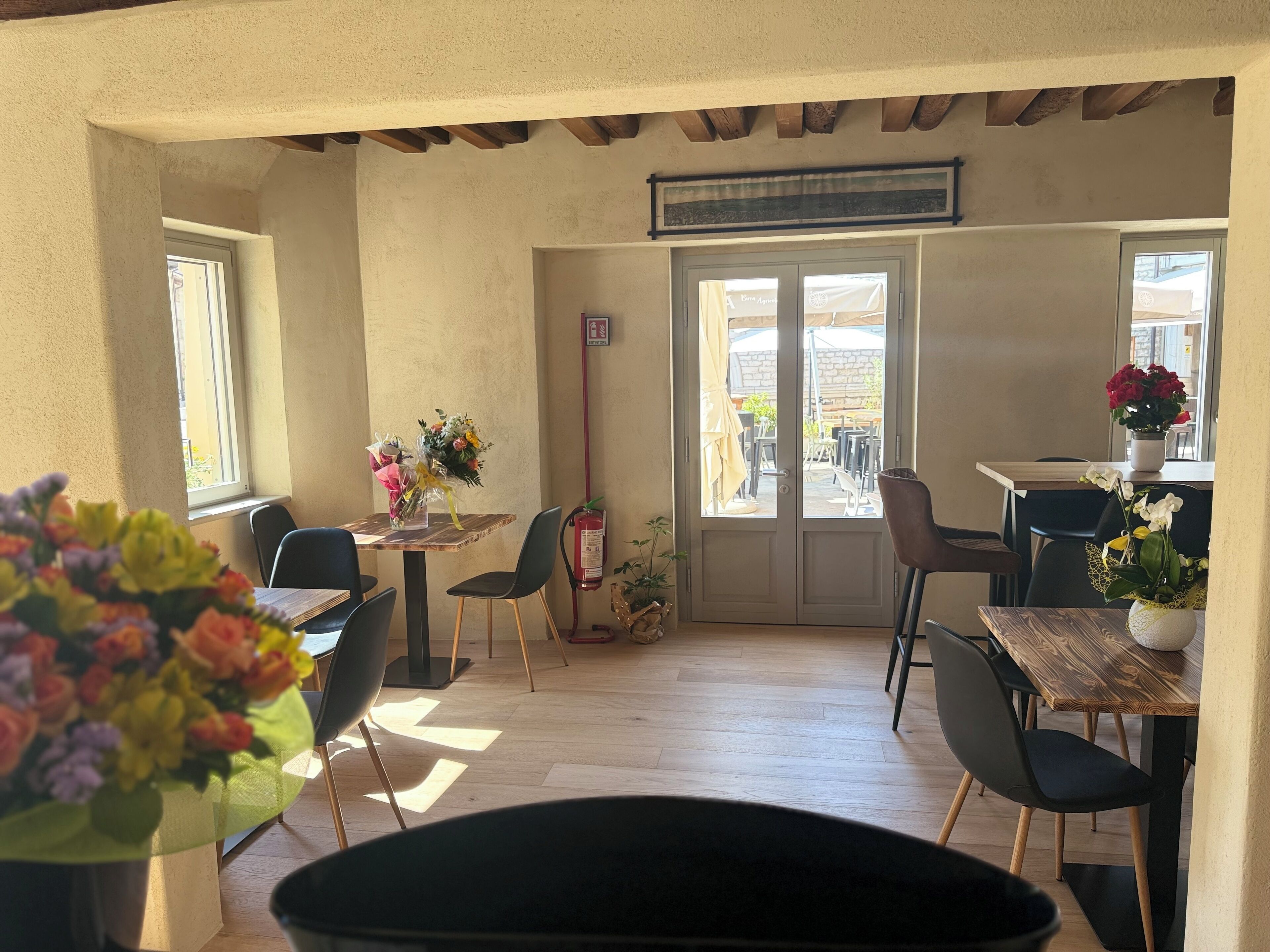 Un espace repas avec des tables et des chaises en bois, un extincteur et une vue à travers les portes vitrées.