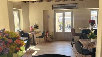 Un espace repas avec des tables et des chaises en bois, un extincteur et une vue à travers les portes vitrées.