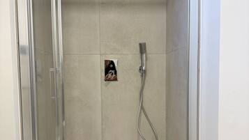 A shower area with a glass door, a handheld showerhead, and a small poster on the wall.