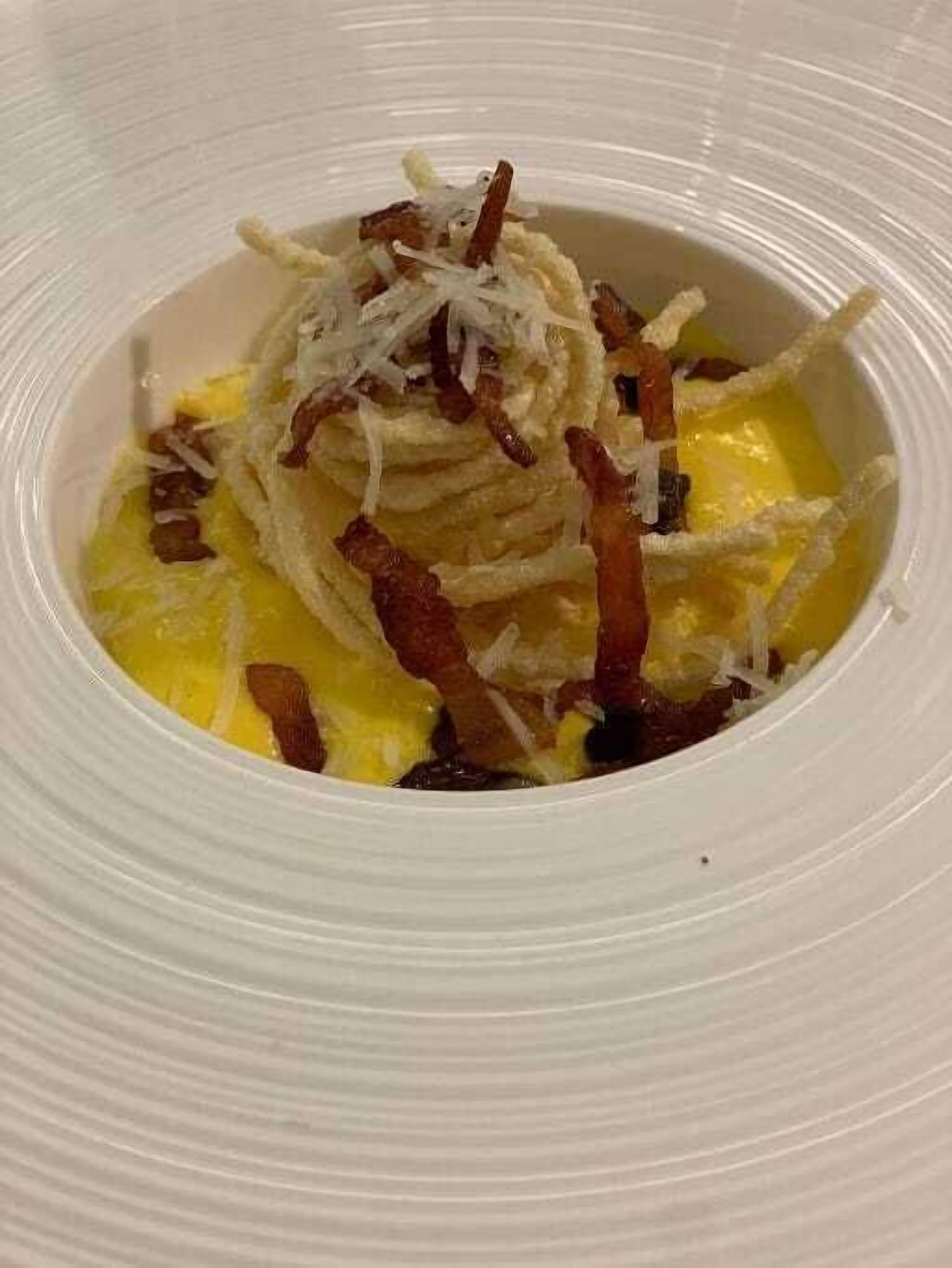 A white plate with a dish containing scrambled eggs, bacon, and shredded cheese.
