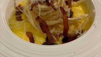 Un plato blanco con un guiso de huevos revueltos, tocino y queso rallado.