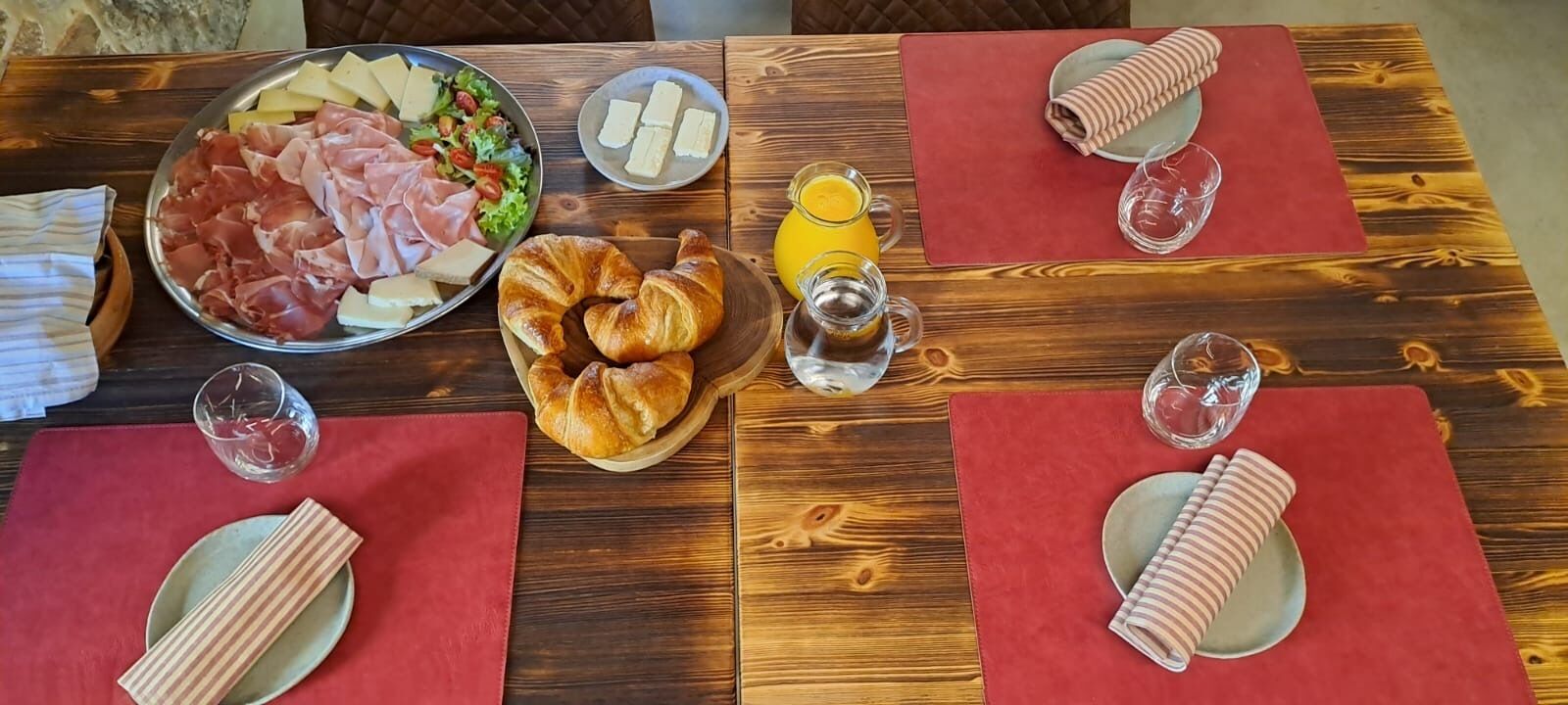 En morgenmadsopstilling med croissanter, ost, skinke og juice på et træbord.