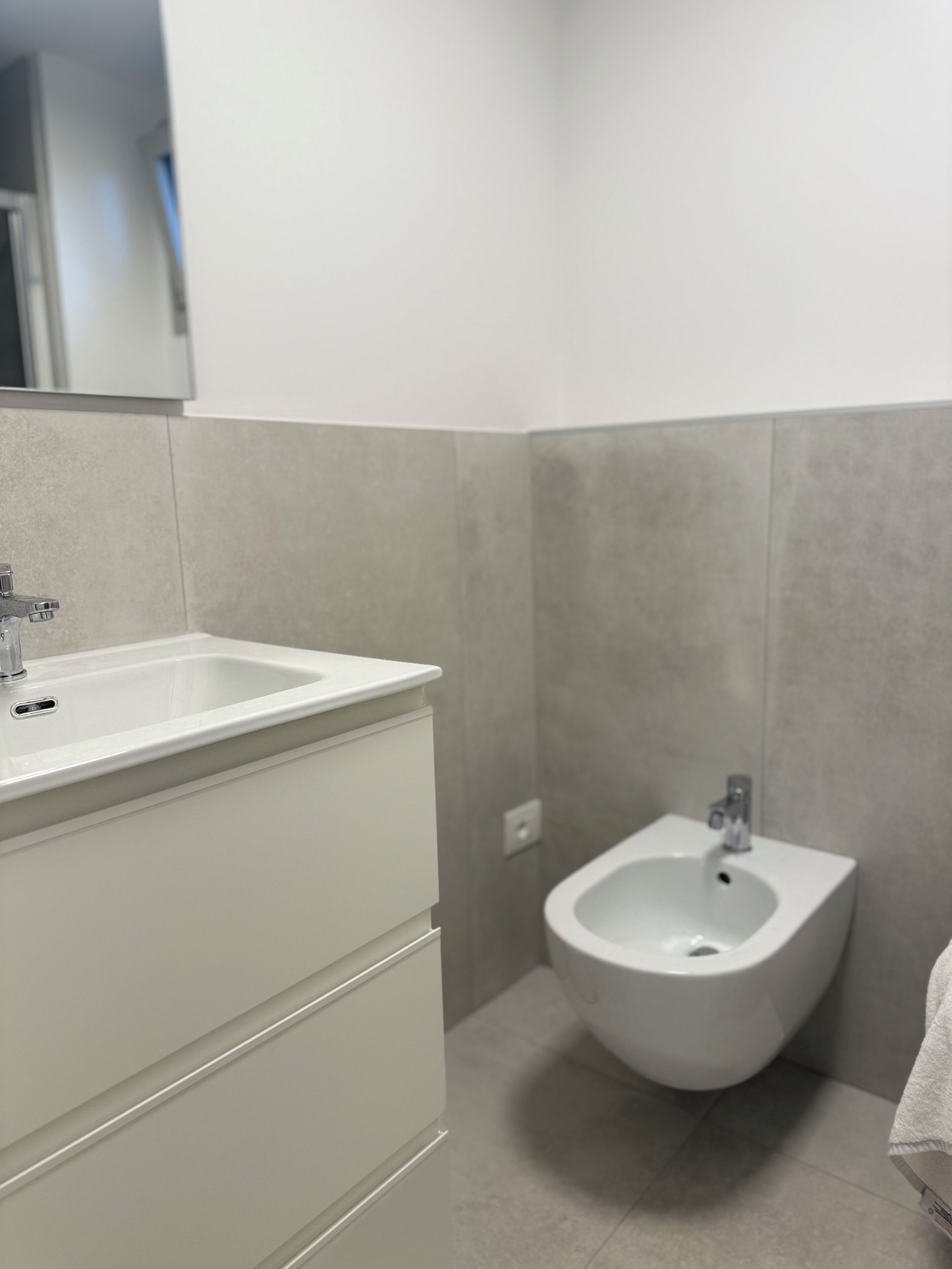 Un bagno moderno con un lavandino bianco, un bidet e pareti rivestite di piastrelle grigie.